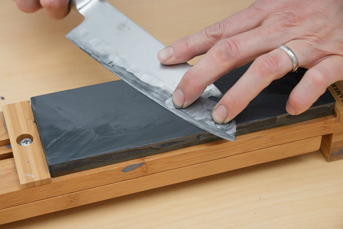 Hands sharpening a knife on a whetstone in a wooden holder